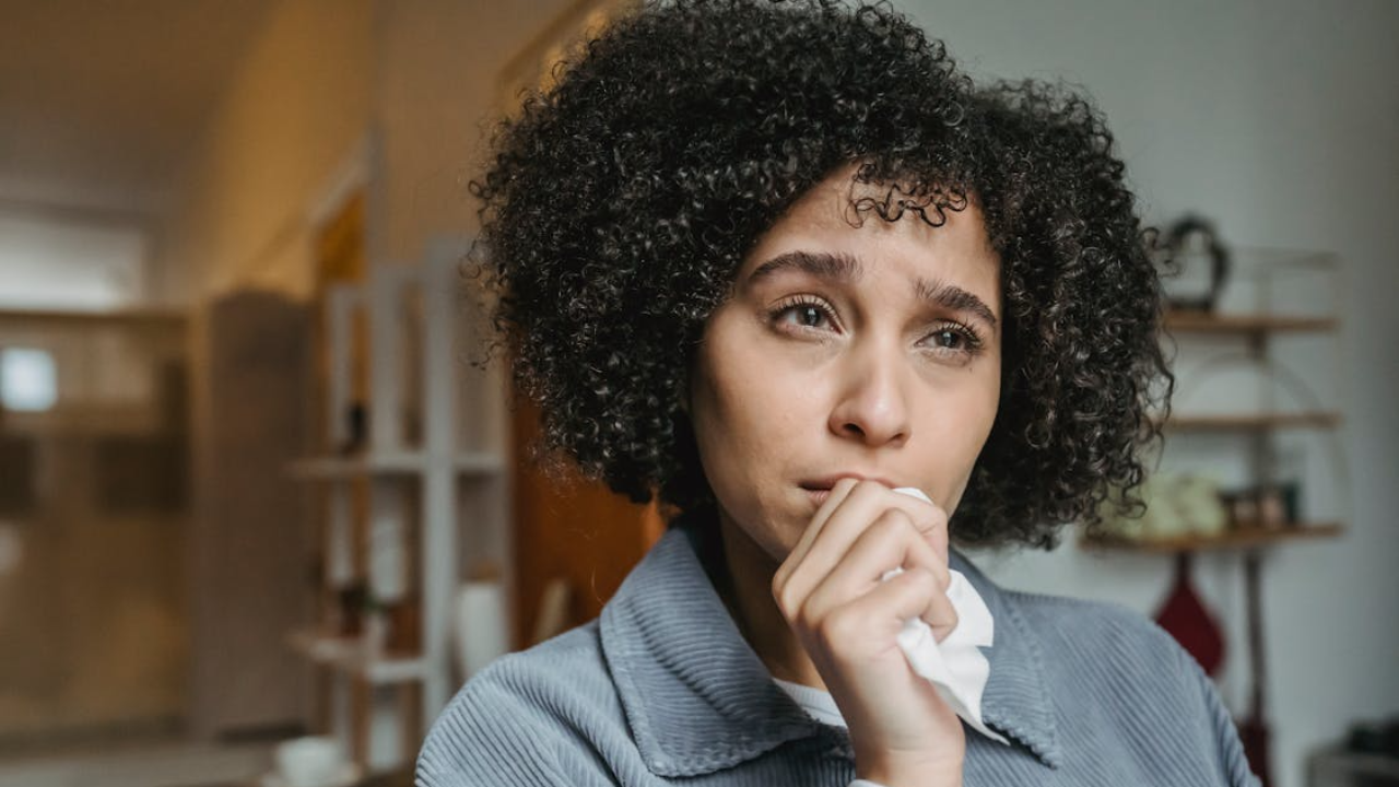 A stressed woman in a light blue sweater gripping her head with both hands.